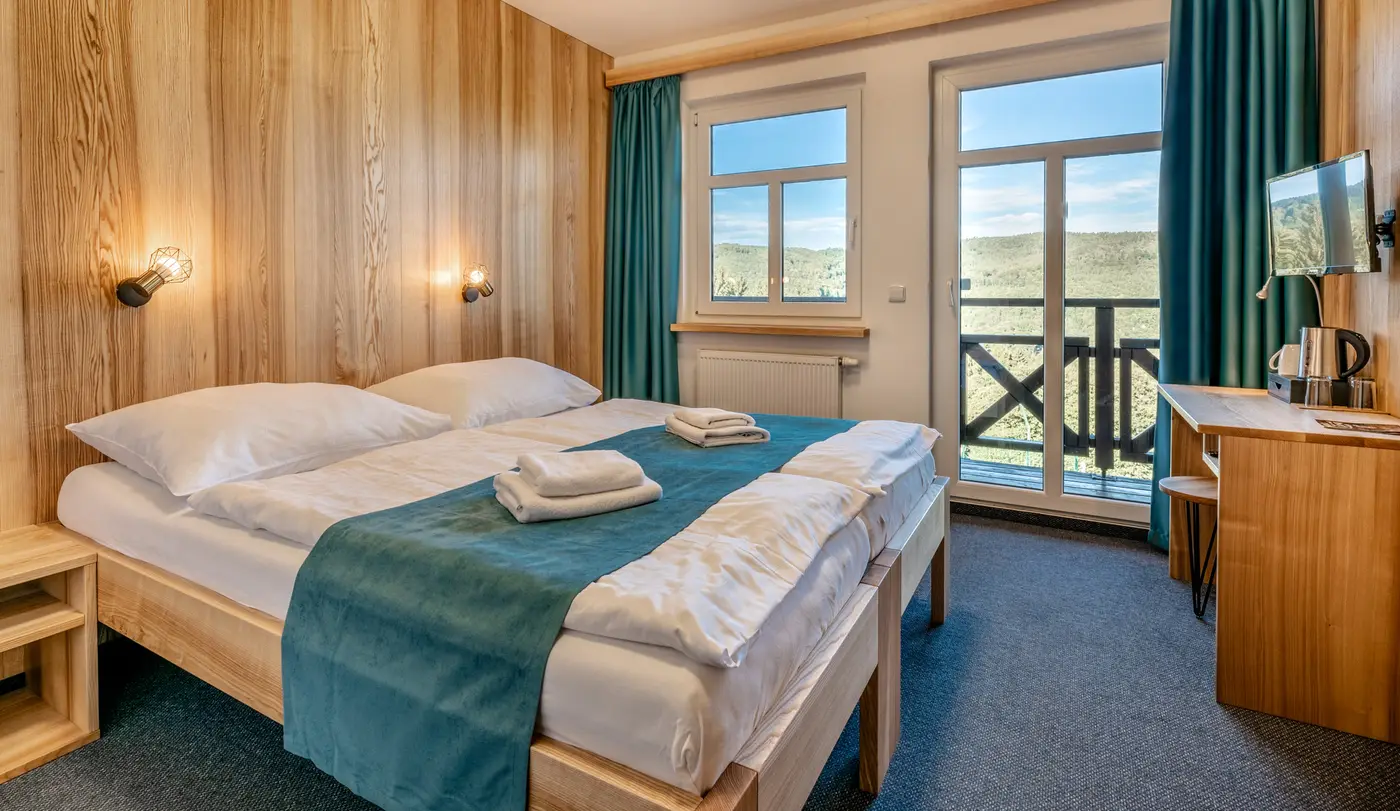 Dvoulůžkový pokoj hotelu Emeran po rekonstrukci, dřevěné obklady a balkon s výhledem do zalesněného údolí